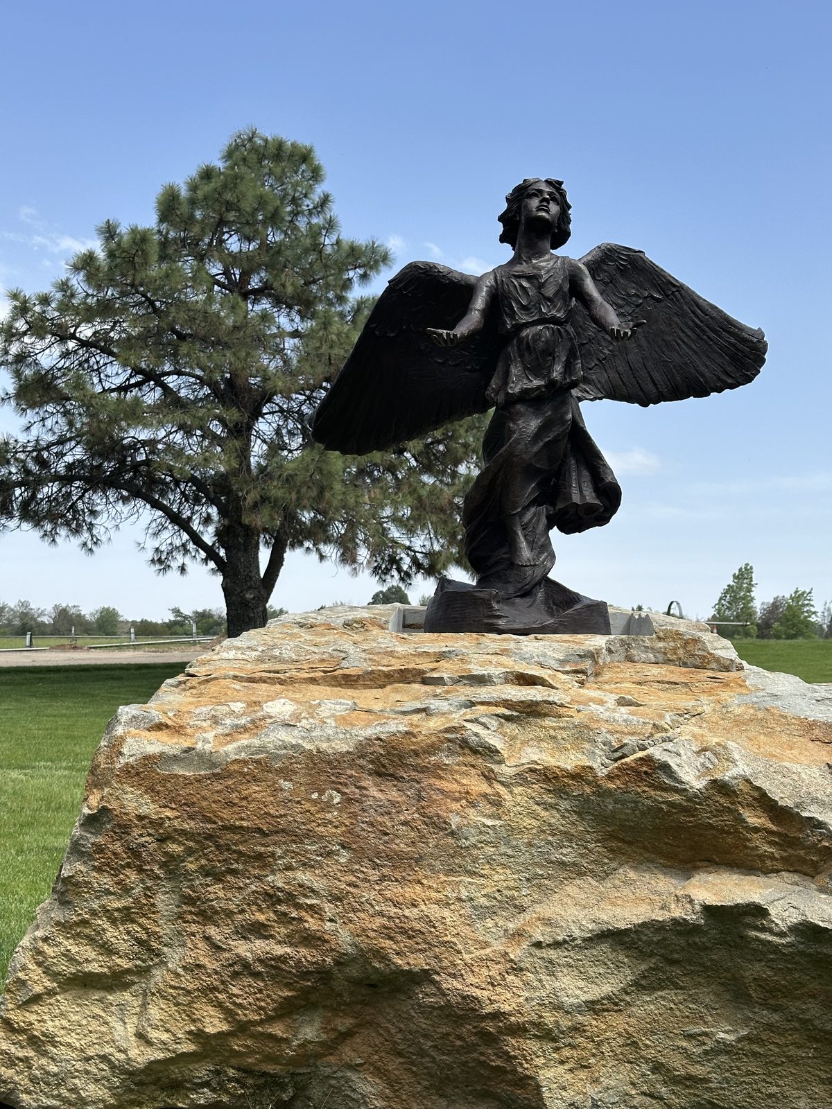 The Angel of Hope statue seen from below against a clear blue sky, framed by pine branches