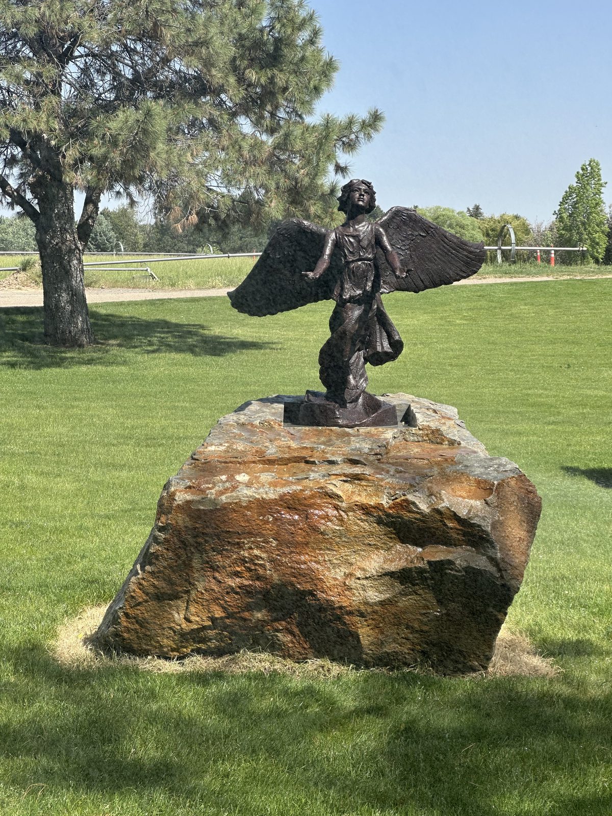 The Angel of Hope statue standing on its large natural stone base, with the cemetery lawn and trees around it